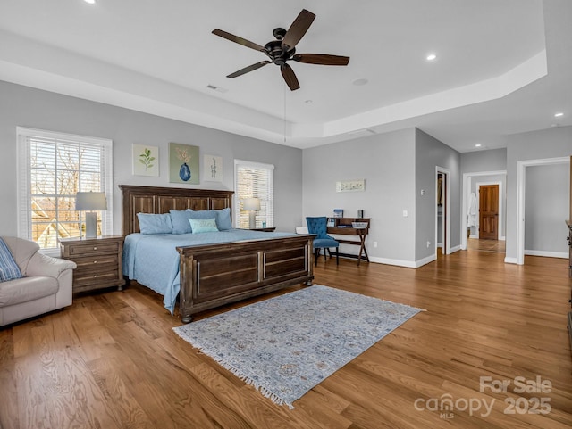 bedroom with ceiling fan, a tray ceiling, and wood-type flooring