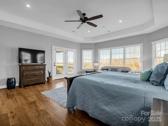 bedroom with ceiling fan, wood-type flooring, a raised ceiling, and access to exterior