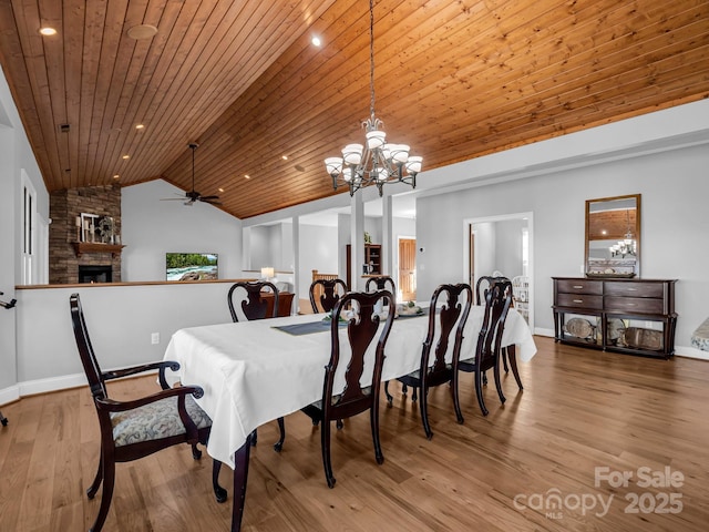 dining room with lofted ceiling, wood ceiling, a stone fireplace, and wood finished floors