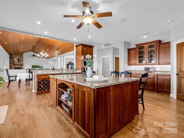 kitchen with lofted ceiling, a peninsula, decorative backsplash, light stone countertops, and light wood finished floors