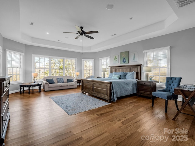 bedroom featuring a tray ceiling, wood finished floors, and visible vents