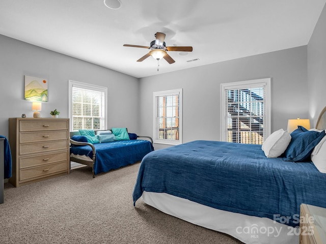 carpeted bedroom with ceiling fan, multiple windows, and visible vents