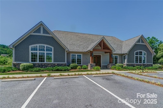 view of front of home with stone siding, a shingled roof, and uncovered parking