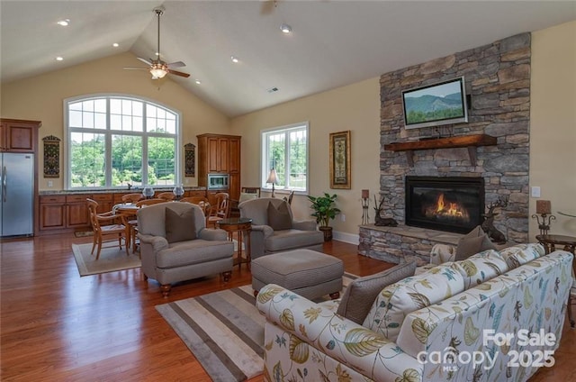 living area featuring high vaulted ceiling, wood finished floors, and a stone fireplace