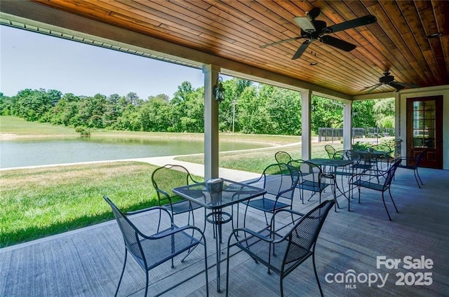 deck featuring ceiling fan, a yard, outdoor dining area, and a water view