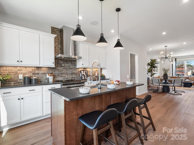 kitchen featuring wall chimney range hood, dark countertops, and light wood-style floors