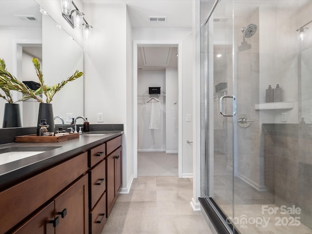 full bath featuring a stall shower, a walk in closet, visible vents, and a sink