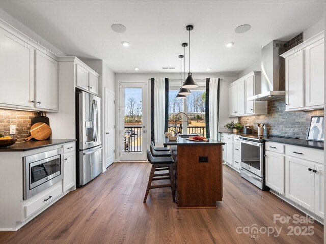kitchen with dark countertops, dark wood-style floors, wall chimney exhaust hood, and appliances with stainless steel finishes