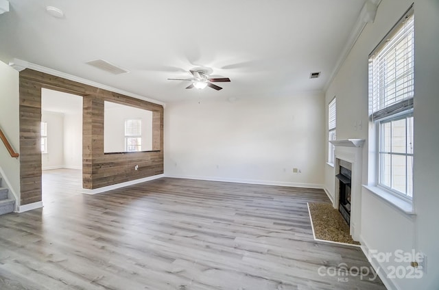 unfurnished living room with crown molding, ceiling fan, wood walls, and light wood-type flooring