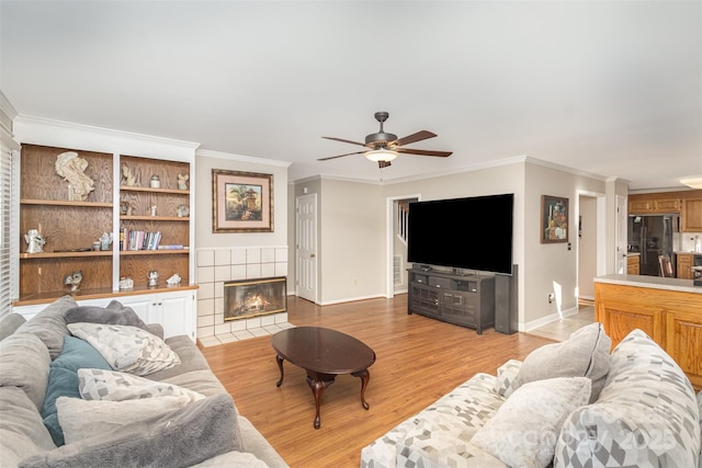 living room featuring a tile fireplace, ceiling fan, light hardwood / wood-style flooring, and ornamental molding