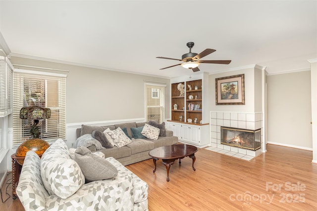 living room featuring built in shelves, ceiling fan, ornamental molding, and a tiled fireplace