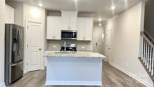 kitchen featuring white cabinetry, light stone counters, stainless steel appliances, and a center island with sink