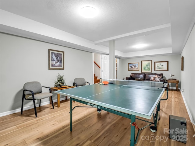 game room with a raised ceiling, a textured ceiling, and light hardwood / wood-style flooring