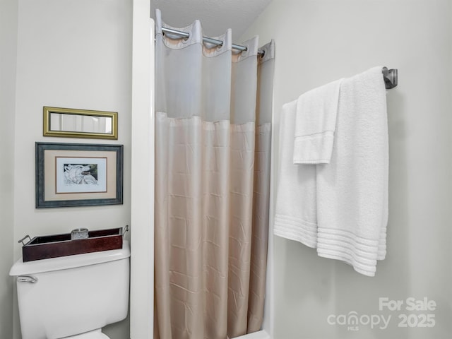 bathroom with curtained shower, toilet, and a textured ceiling