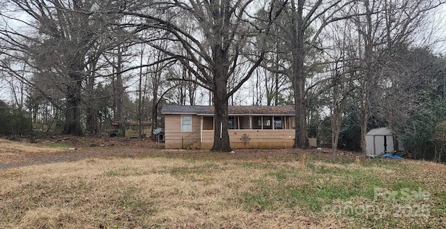 view of front of house with a sunroom, a shed, and a front lawn