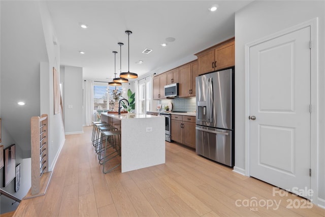 kitchen with stainless steel appliances, tasteful backsplash, a center island with sink, and light wood-style floors