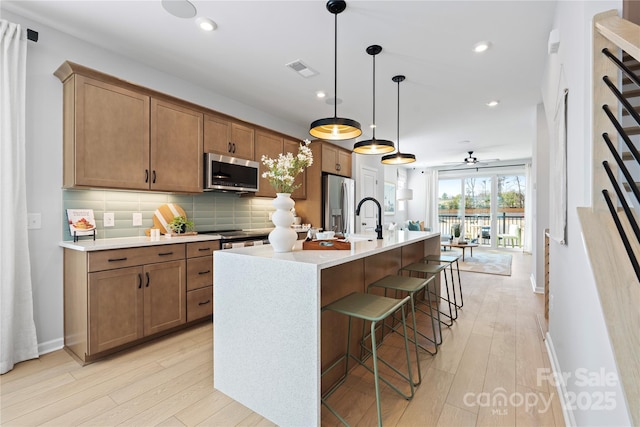 kitchen featuring stainless steel appliances, light wood finished floors, backsplash, and a center island with sink