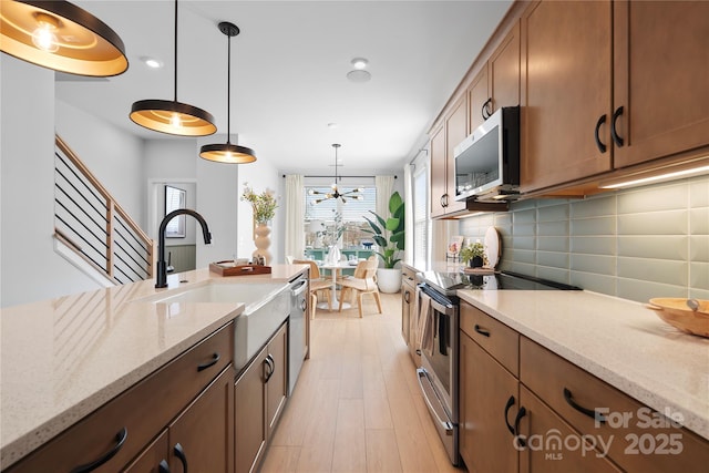 kitchen with light stone counters, a sink, appliances with stainless steel finishes, tasteful backsplash, and decorative light fixtures