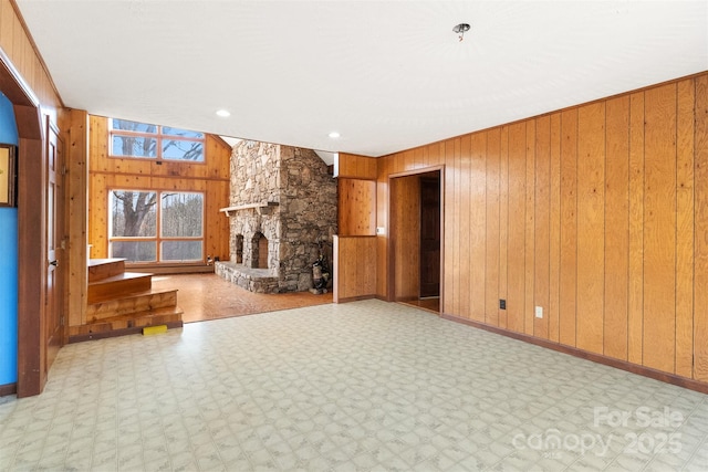 unfurnished living room with a stone fireplace and wood walls