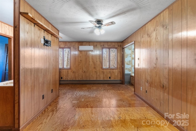 spare room with wood walls, an AC wall unit, ceiling fan, a textured ceiling, and a baseboard radiator