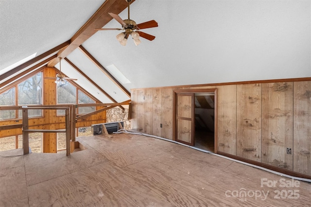 interior space with ceiling fan, lofted ceiling with skylight, a textured ceiling, and wooden walls