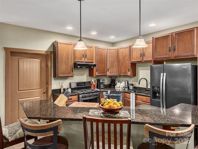 kitchen with a breakfast bar area, stainless steel appliances, under cabinet range hood, a sink, and brown cabinetry