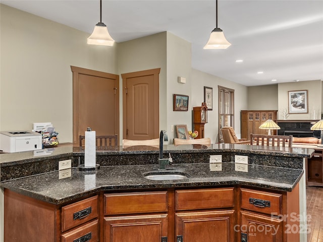kitchen featuring a sink, brown cabinets, open floor plan, dark stone countertops, and decorative light fixtures