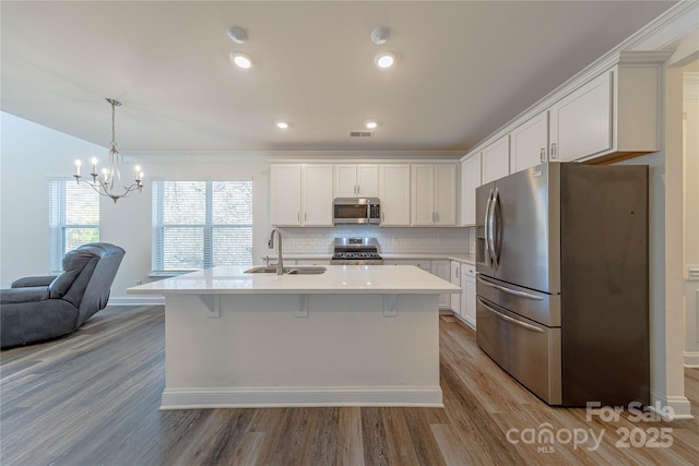 kitchen with stainless steel appliances, sink, pendant lighting, white cabinetry, and an island with sink