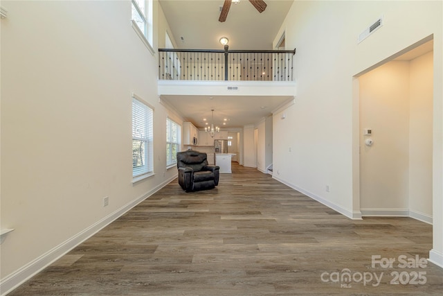 interior space with hardwood / wood-style floors, ceiling fan with notable chandelier, and a high ceiling