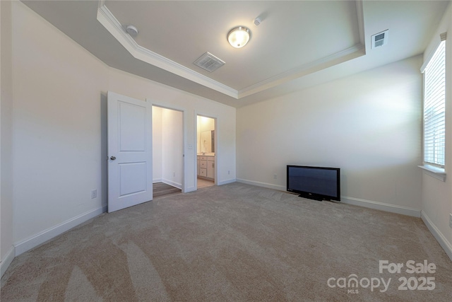 unfurnished bedroom featuring light carpet, ensuite bathroom, crown molding, and a tray ceiling