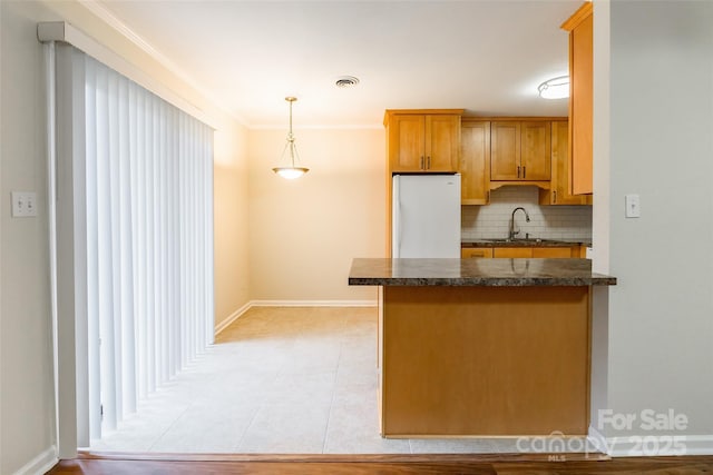 kitchen featuring sink, hanging light fixtures, kitchen peninsula, white fridge, and backsplash