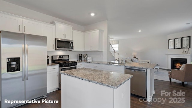 kitchen with sink, a kitchen island, light stone counters, white cabinetry, and stainless steel appliances