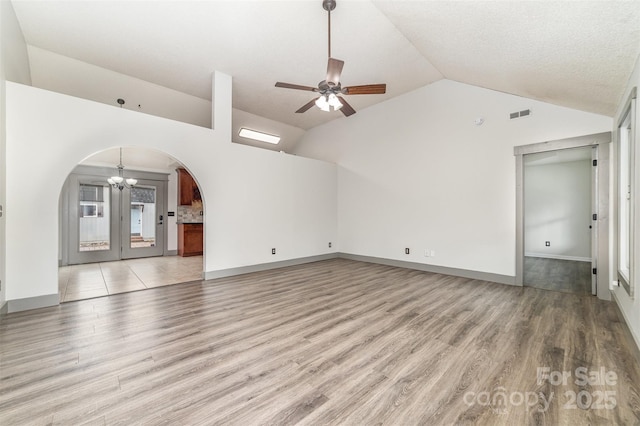 unfurnished living room featuring light hardwood / wood-style flooring, ceiling fan with notable chandelier, and vaulted ceiling