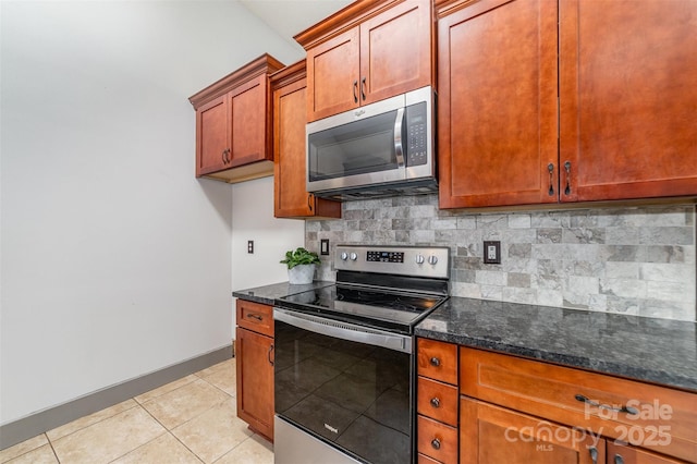 kitchen with backsplash, stainless steel appliances, light tile patterned floors, and dark stone countertops