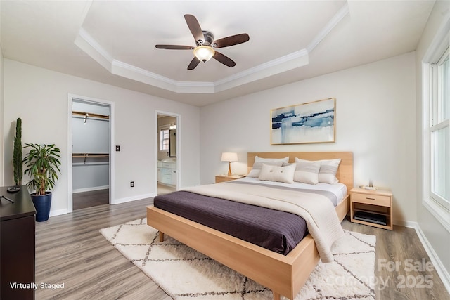 bedroom featuring hardwood / wood-style flooring, a walk in closet, ornamental molding, and a raised ceiling