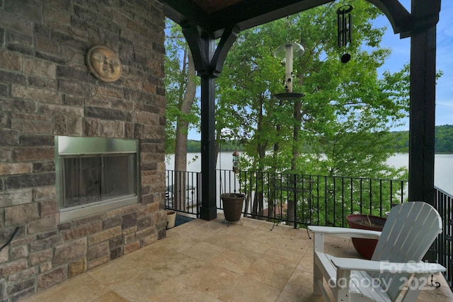 view of patio with a water view and an outdoor stone fireplace