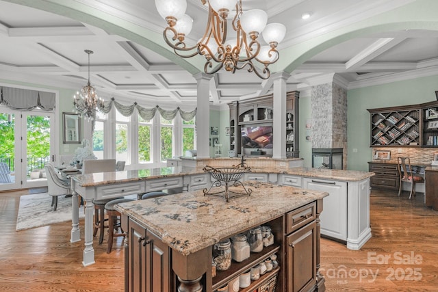 kitchen with pendant lighting, a kitchen island, a stone fireplace, and coffered ceiling