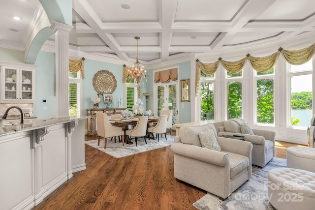 sunroom featuring ornate columns, a wealth of natural light, coffered ceiling, and an inviting chandelier