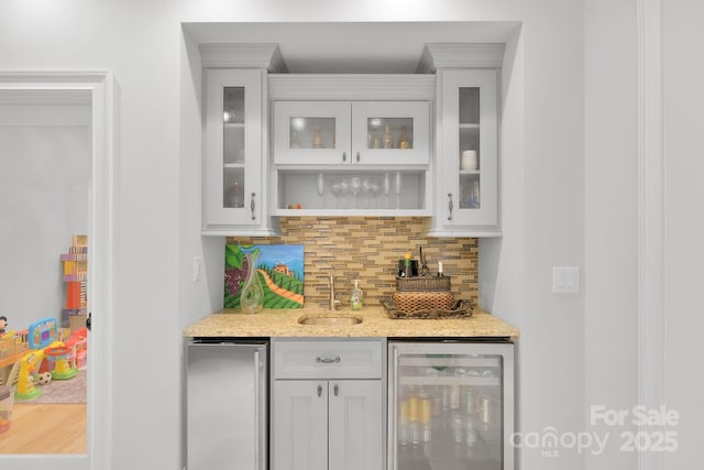 bar with decorative backsplash, sink, white cabinets, wine cooler, and fridge