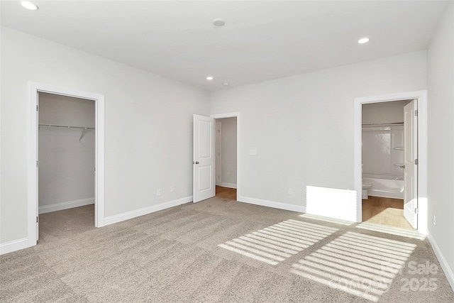 unfurnished bedroom with connected bathroom, a spacious closet, light carpet, and a closet