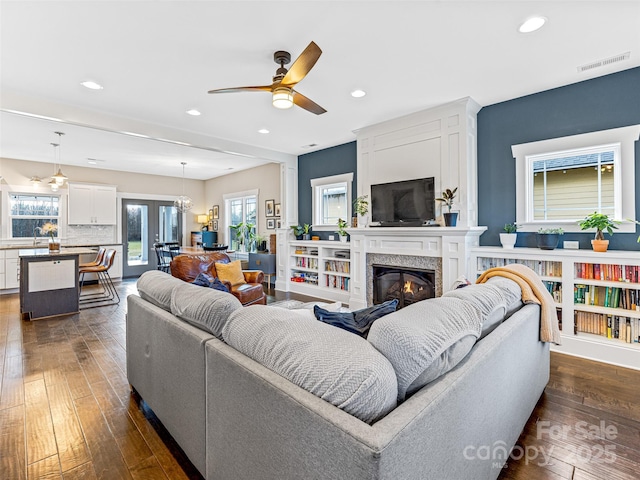 living room with a high end fireplace, dark hardwood / wood-style flooring, and ceiling fan