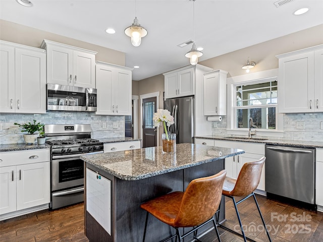 kitchen featuring white cabinetry, sink, stainless steel appliances, decorative light fixtures, and a kitchen island