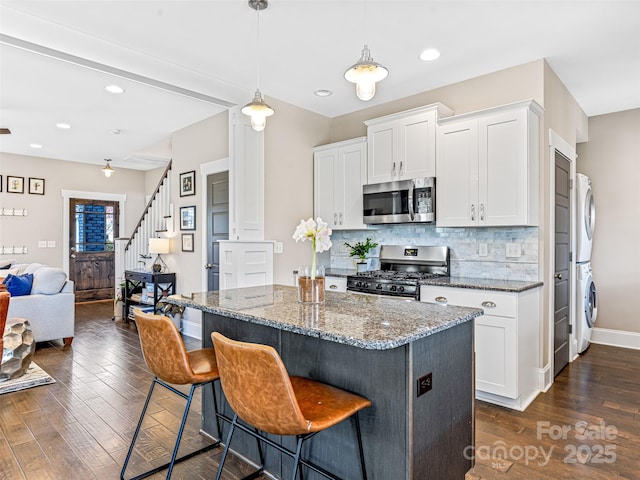 kitchen with dark stone countertops, white cabinetry, appliances with stainless steel finishes, and stacked washer and clothes dryer