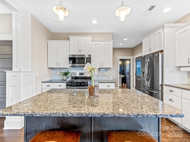 kitchen with a center island, backsplash, white cabinets, light stone countertops, and appliances with stainless steel finishes