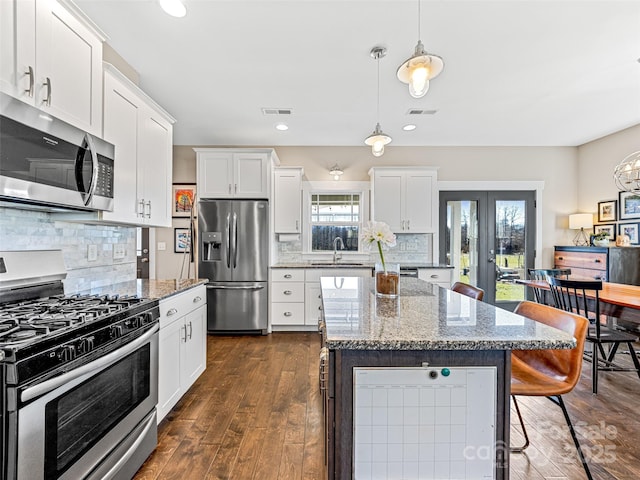 kitchen featuring decorative backsplash, white cabinetry, stainless steel appliances, and decorative light fixtures