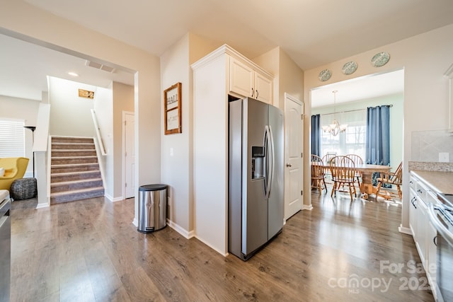 kitchen with stainless steel refrigerator with ice dispenser, backsplash, pendant lighting, hardwood / wood-style floors, and white cabinetry