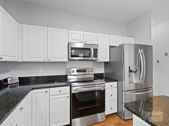 kitchen with light hardwood / wood-style floors, dark stone counters, white cabinets, and appliances with stainless steel finishes