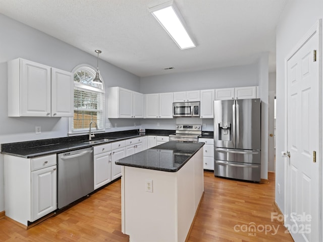 kitchen with sink, appliances with stainless steel finishes, white cabinetry, a kitchen island, and decorative light fixtures