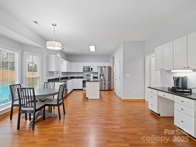 kitchen with decorative light fixtures, a center island, light hardwood / wood-style flooring, appliances with stainless steel finishes, and white cabinets