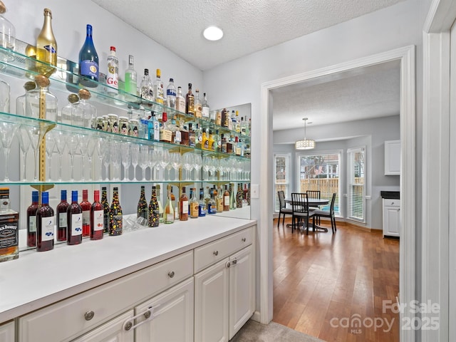 bar with hanging light fixtures, a textured ceiling, hardwood / wood-style floors, and white cabinets